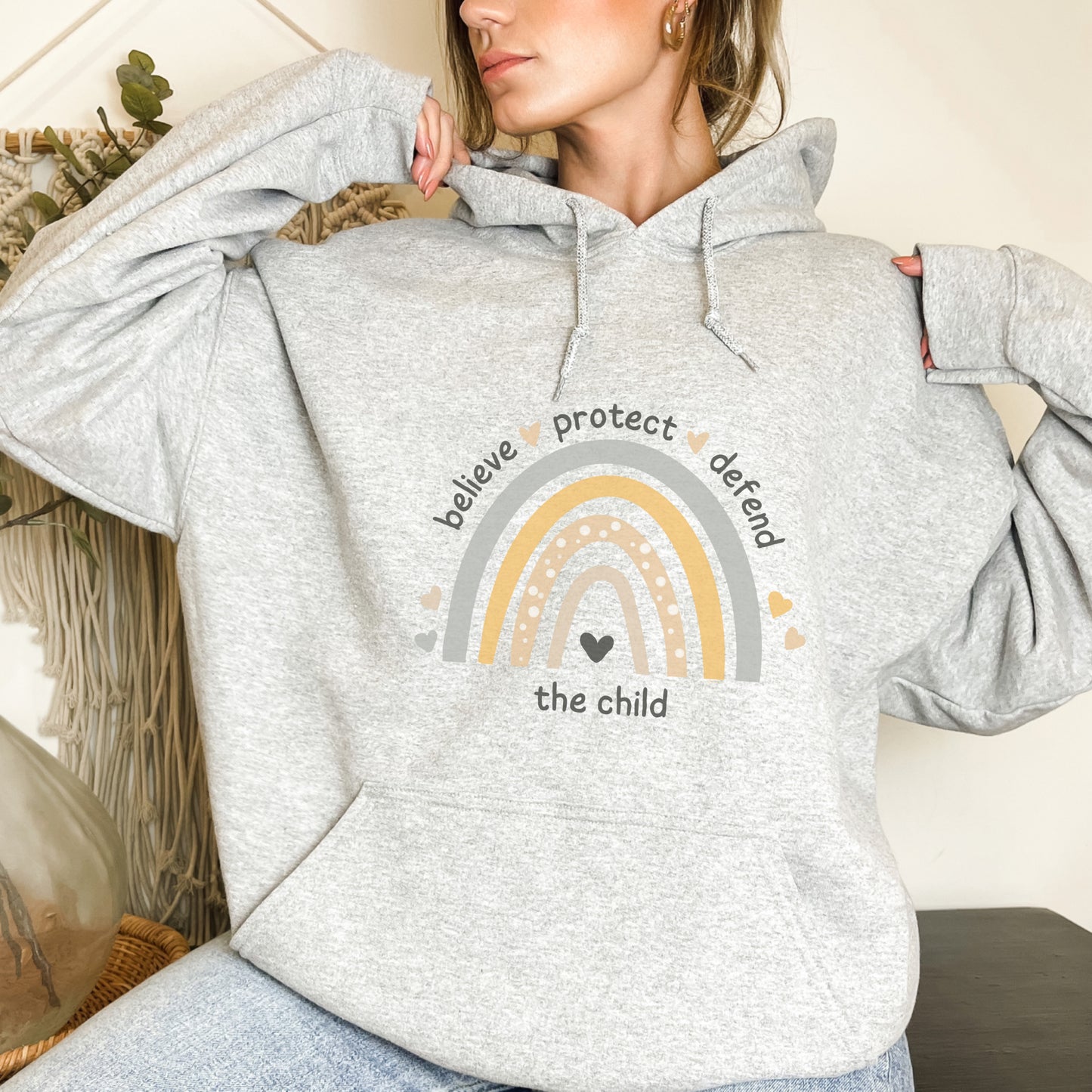 The front of the sweatshirt proudly displays a boho rainbow with the phrase "Believe Protect Defend The Child” in a whimsical and eye-catching font. A powerful message that underscores the importance of safeguarding children's rights and well-being.