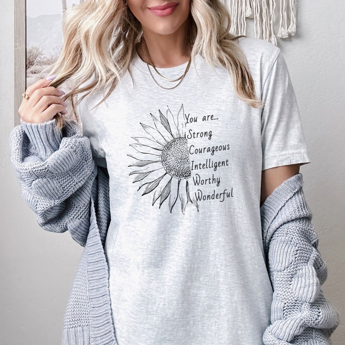 This thoughtfully designed shirt features a vibrant sunflower, symbolizing resilience and growth, accompanied by the powerful mantra: "You are strong, courageous, intelligent, worthy, and wonderful."