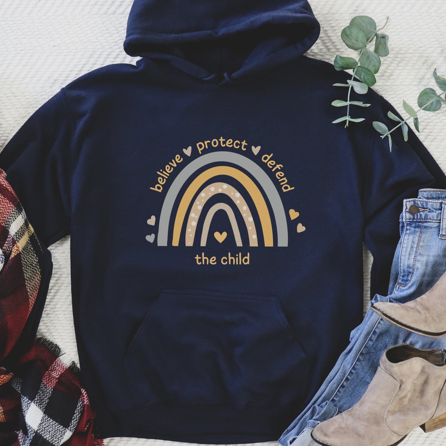 The front of the sweatshirt proudly displays a boho rainbow with the phrase "Believe Protect Defend The Child” in a whimsical and eye-catching font. A powerful message that underscores the importance of safeguarding children's rights and well-being.