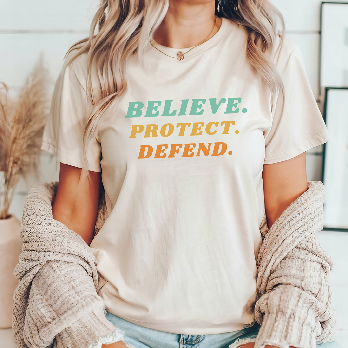 Bella Canvas T-shirt in the color Natural with bold retro text in green, yellow, and orange that reads: Believe. Protect. Defend.