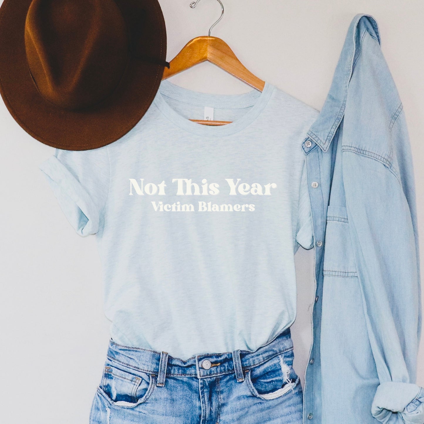 The front of the sweatshirt proudly displays the phrase "Not This Year Victim Blamers" in a bold and eye-catching font. This message serves as a reminder that we reject victim-blaming and support those who have faced injustice.