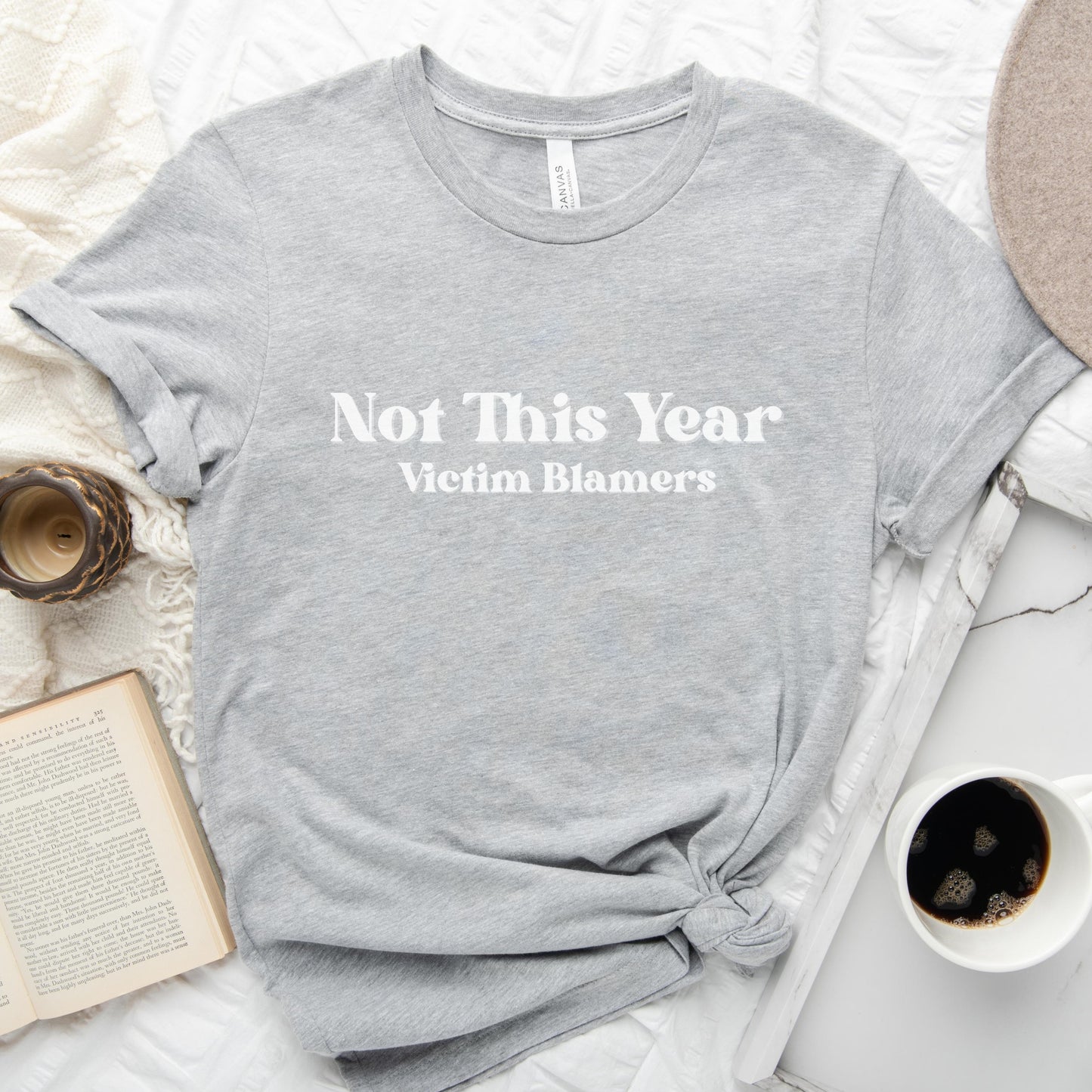 The front of the sweatshirt proudly displays the phrase "Not This Year Victim Blamers" in a bold and eye-catching font. This message serves as a reminder that we reject victim-blaming and support those who have faced injustice.