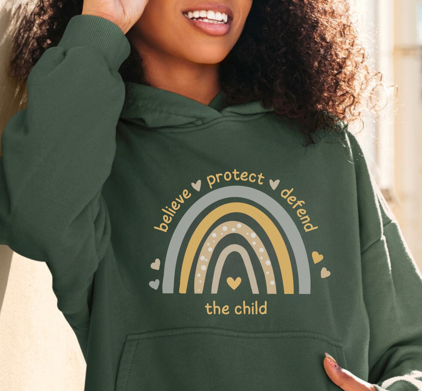 The front of the sweatshirt proudly displays a boho rainbow with the phrase "Believe Protect Defend The Child” in a whimsical and eye-catching font. A powerful message that underscores the importance of safeguarding children's rights and well-being.