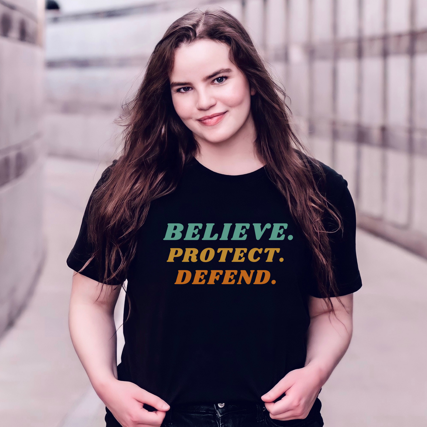 Black Bella Canvas T-shirt with bold retro text in green, yellow, and orange that reads: Believe. Protect. Defend.