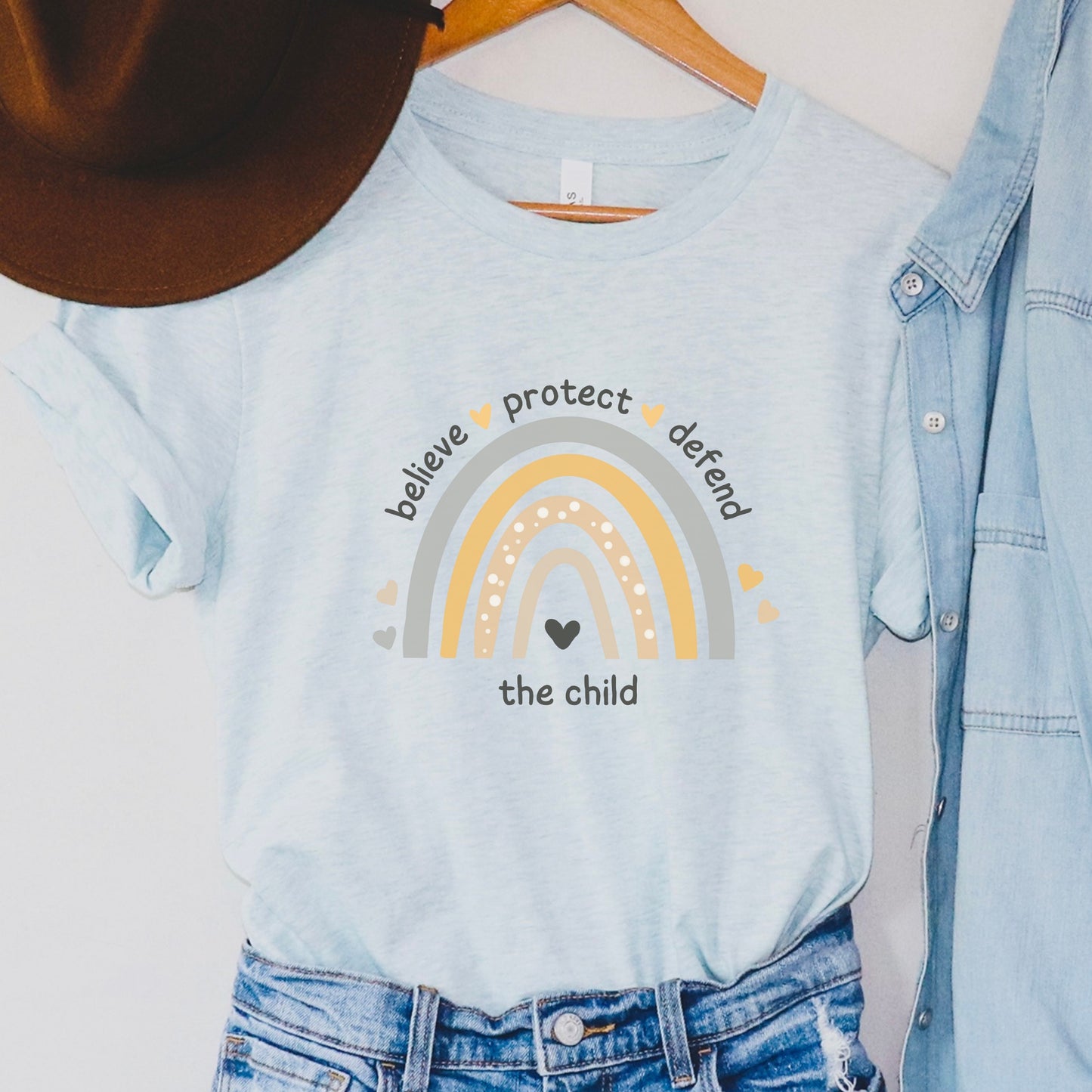 The front of the tee displays a boho rainbow with the phrase Believe Protect Defend The Child. A powerful message that underscores the importance of safeguarding children's rights and well being. Perfect for child advocates and Child Abuse Awareness and Prevention Month (CAAPM)
