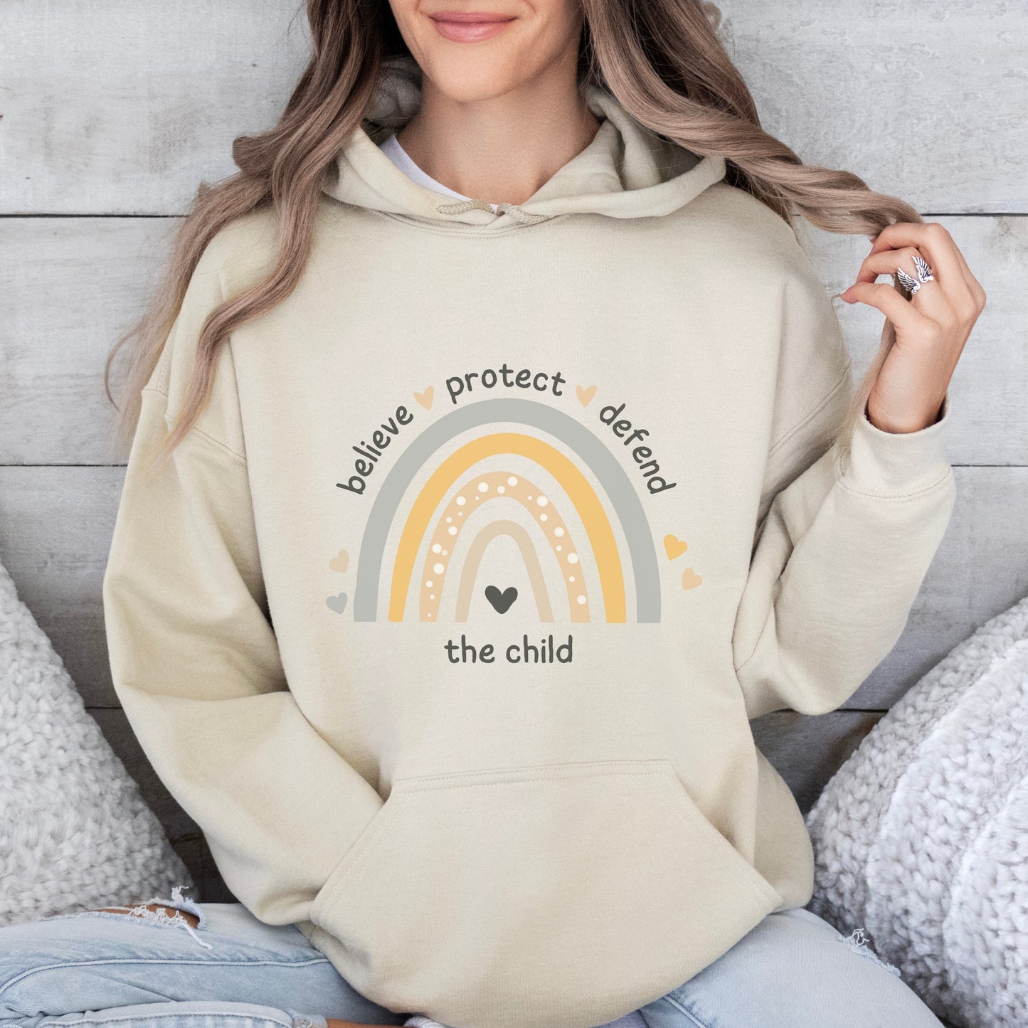 The front of the sweatshirt proudly displays a boho rainbow with the phrase "Believe Protect Defend The Child” in a whimsical and eye-catching font. A powerful message that underscores the importance of safeguarding children's rights and well-being.