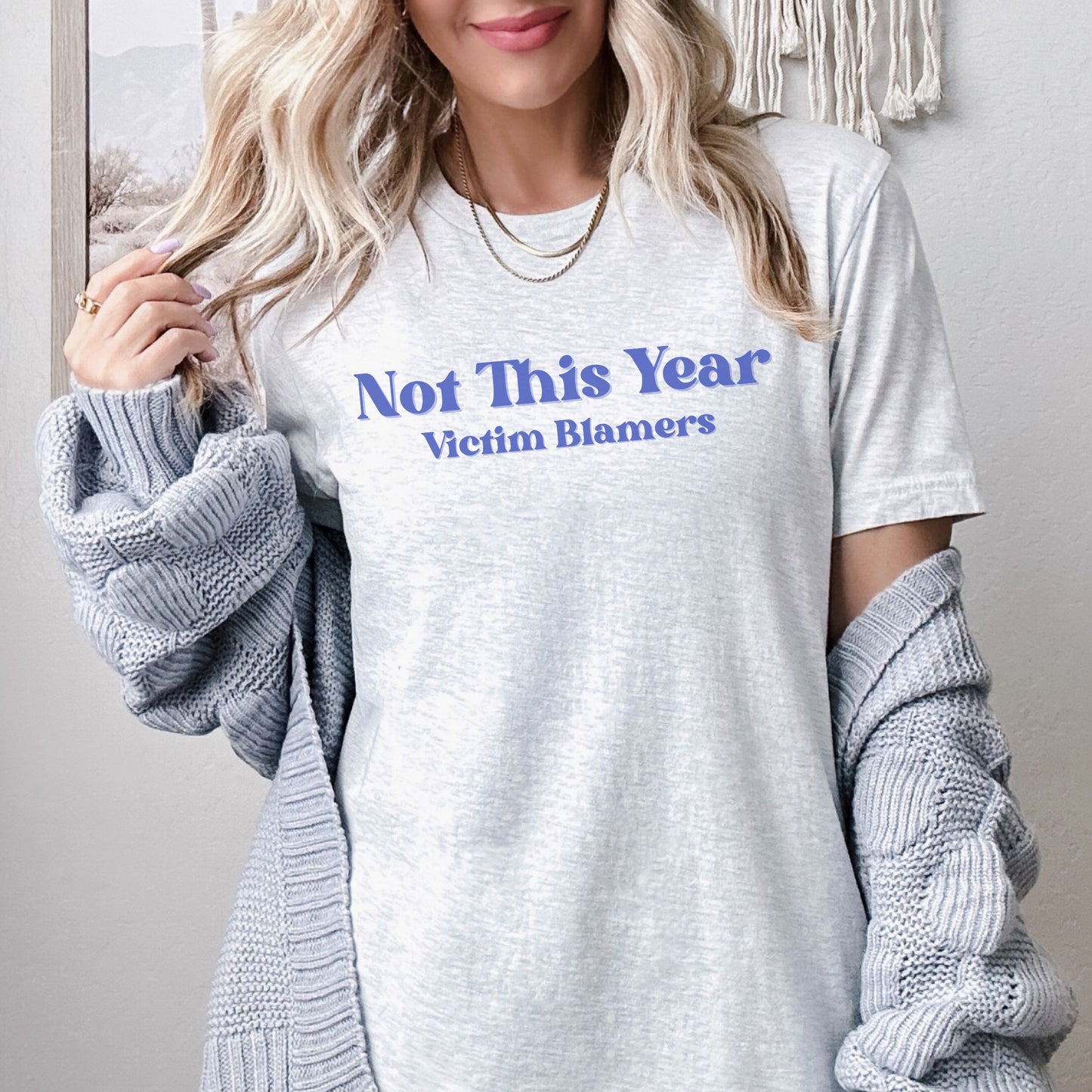 The front of the sweatshirt proudly displays the phrase "Not This Year Victim Blamers" in a bold and eye-catching font. This message serves as a reminder that we reject victim-blaming and support those who have faced injustice.