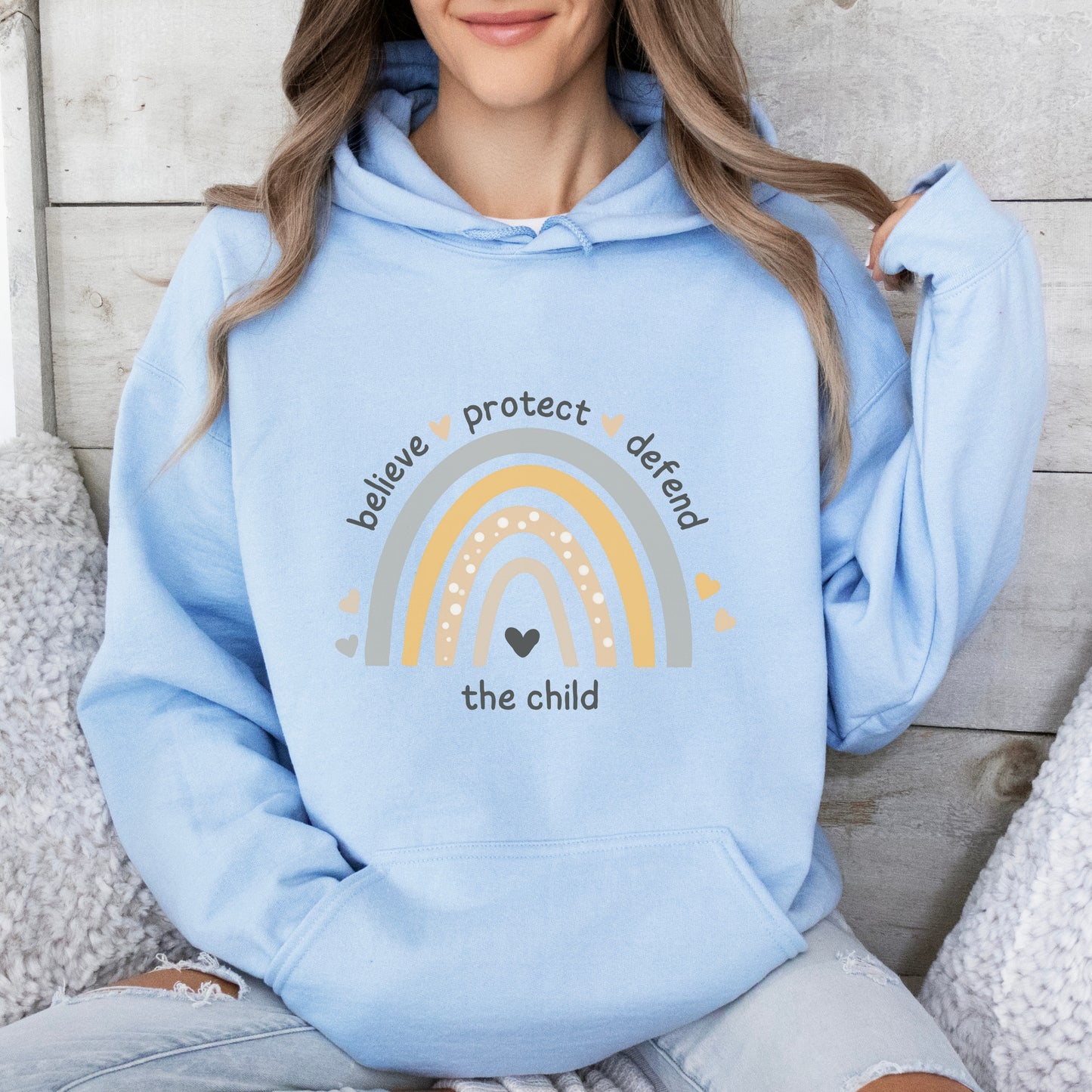 The front of the sweatshirt proudly displays a boho rainbow with the phrase "Believe Protect Defend The Child” in a whimsical and eye-catching font. A powerful message that underscores the importance of safeguarding children's rights and well-being.