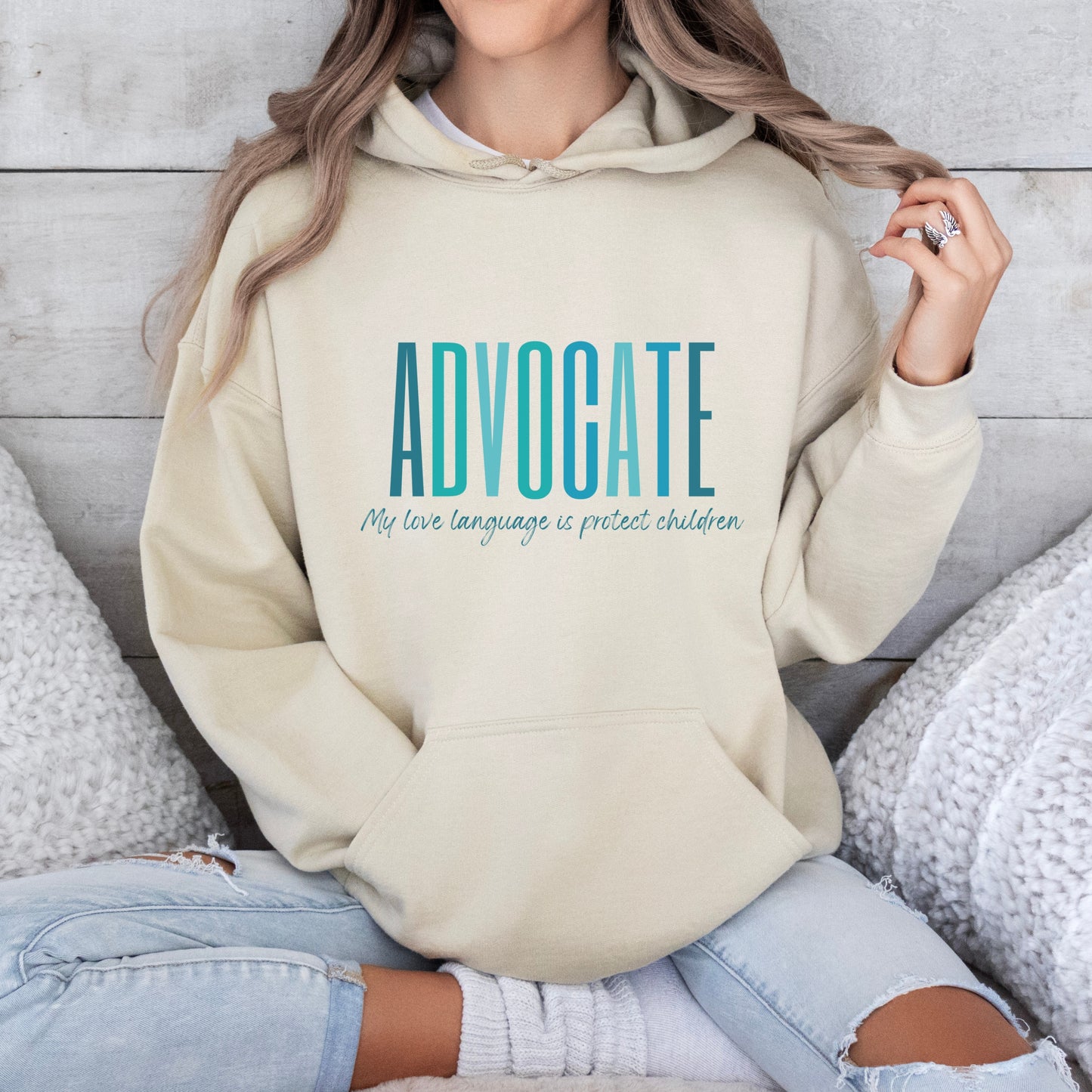 Front and center of this hooded sweatshirt, the bold message declares, "ADVOCATE: my love language is protect children." Artfully designed in varying shades of blue, this impactful phrase encapsulates the essence of your commitment to safeguarding children and promoting their well-being. Perfect for child advocates, champions of children’s mental health, and for Child Abuse Awareness and Prevention Month
