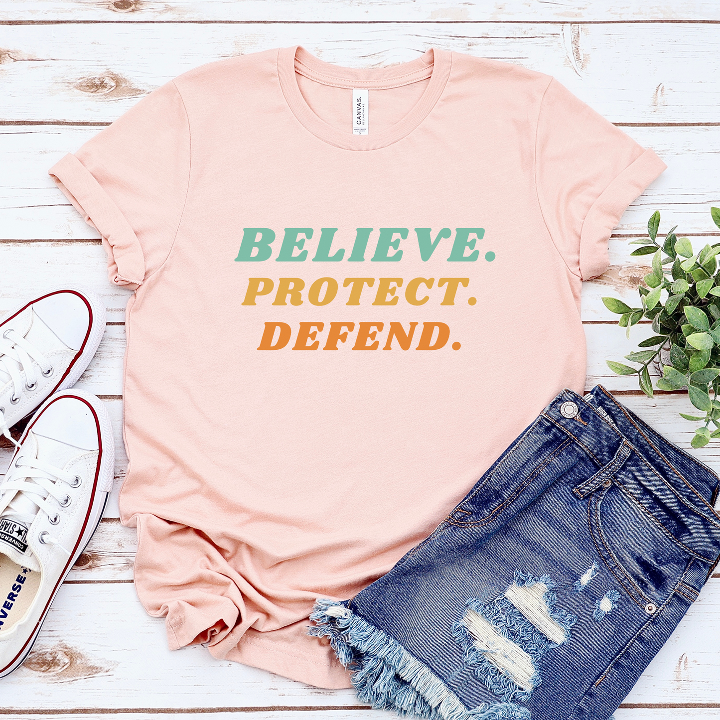 Heather Peach Bella Canvas T-shirt with bold retro text in green, yellow, and orange that reads: Believe. Protect. Defend.
