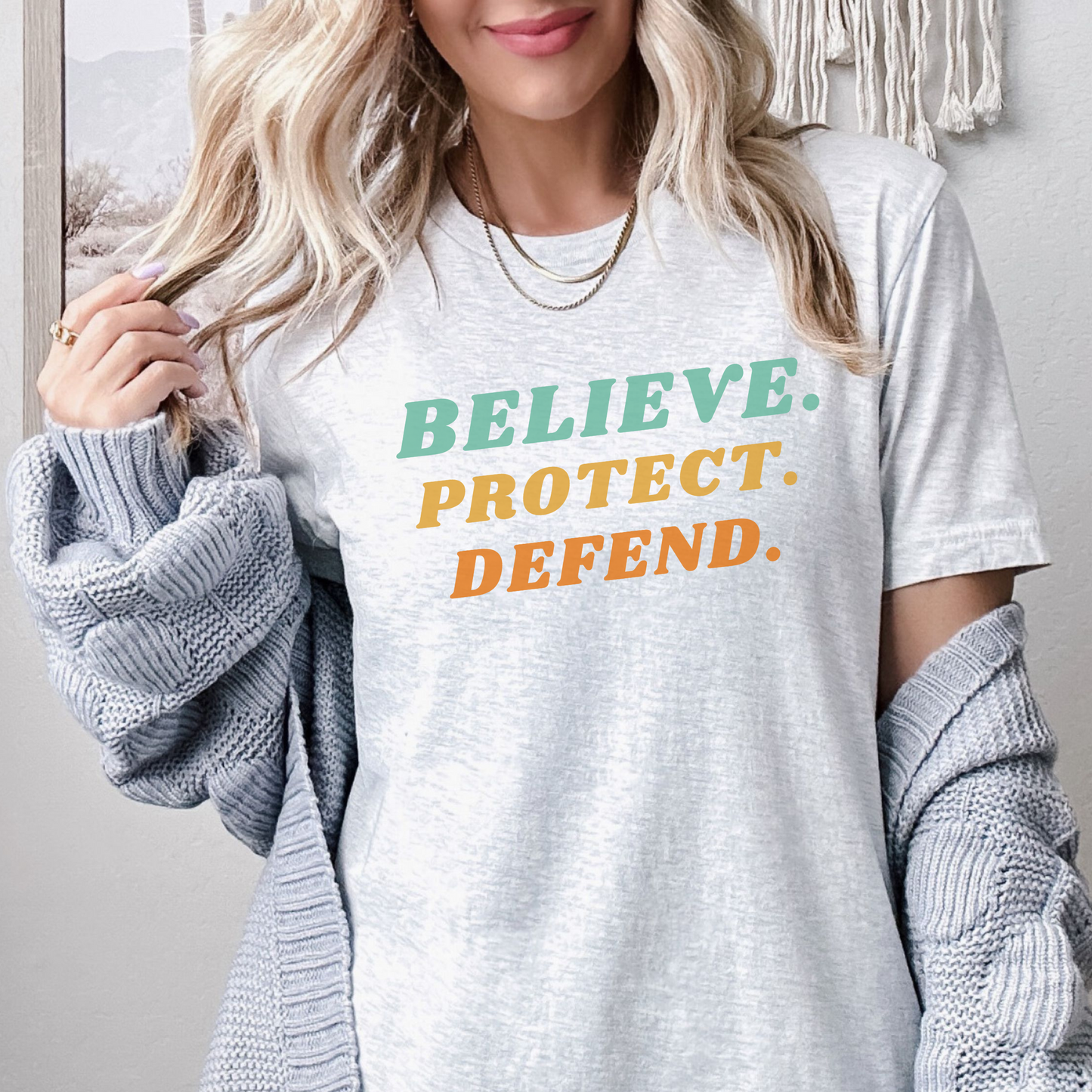 Ash Bella Canvas T-shirt with bold retro text in green, yellow, and orange that reads: Believe. Protect. Defend.