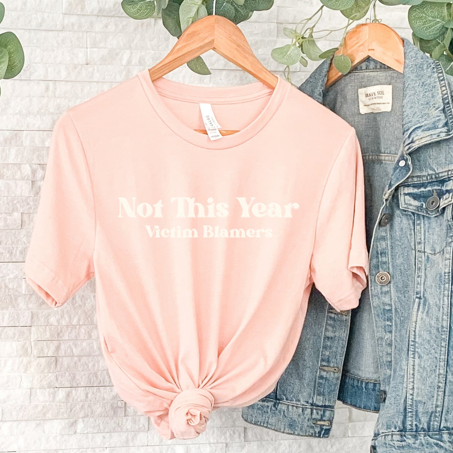 The front of the sweatshirt proudly displays the phrase "Not This Year Victim Blamers" in a bold and eye-catching font. This message serves as a reminder that we reject victim-blaming and support those who have faced injustice.