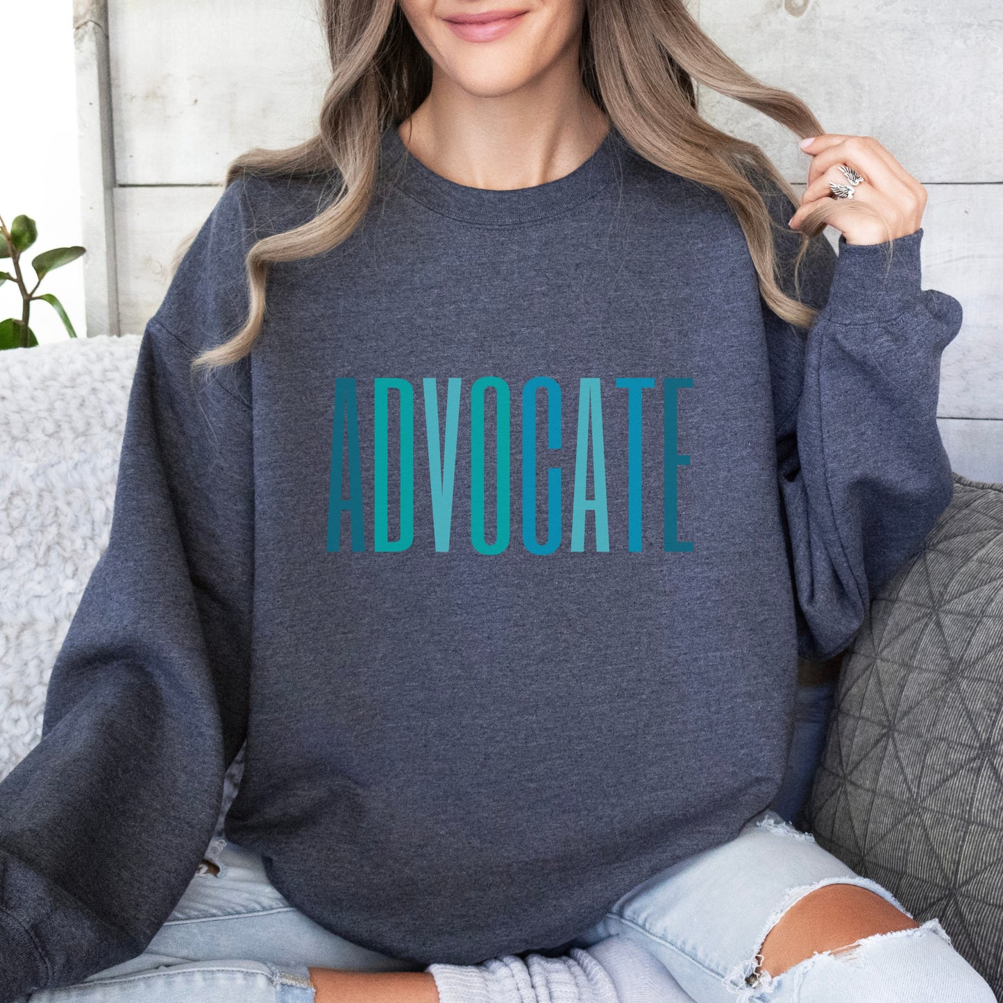 The front of the sweatshirt proudly displays the word ADVOCATE in a bold and eye catching font in varying shades of blue which is the color of child advocacy. It is a wearable symbol of your dedication to a world where all children are loved, cherished, and protected.
