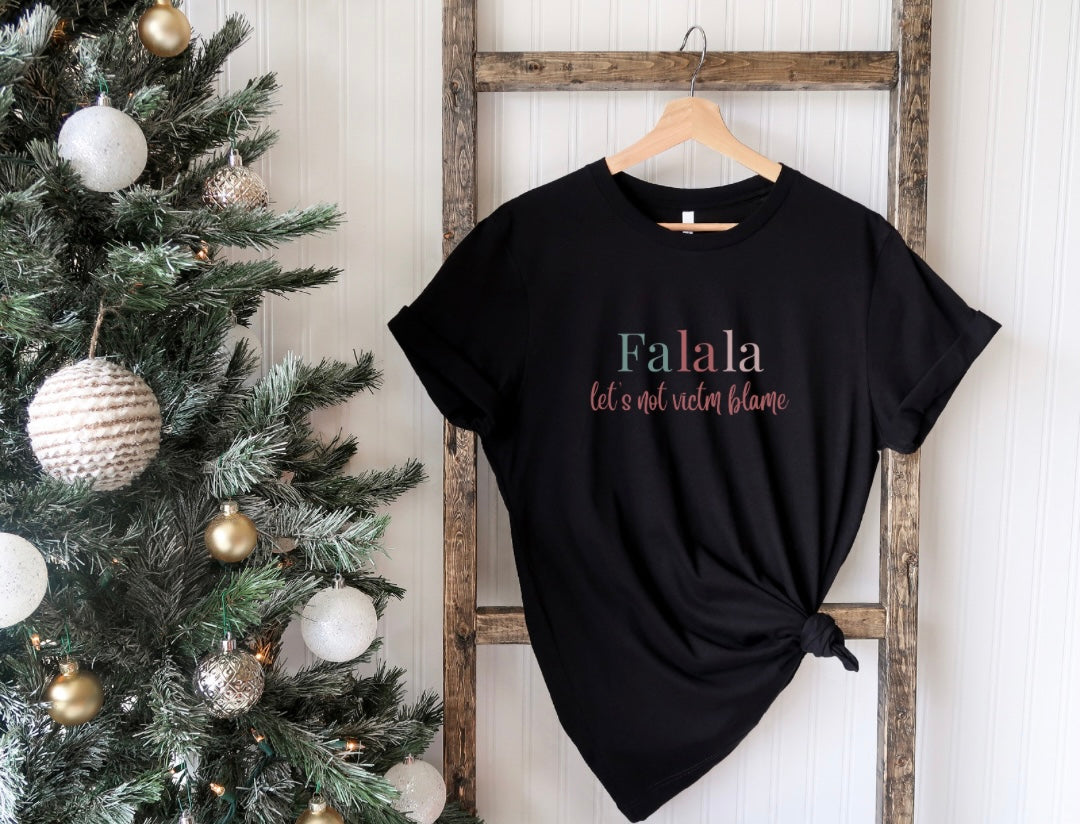 Empowerment-themed holiday T-shirt with festive trending colors design and the powerful statement 'Fa la la, Let's Not Victim Blame.' Ideal for advocates and survivors of abuse, this tee promotes empathy and awareness during the holiday season.