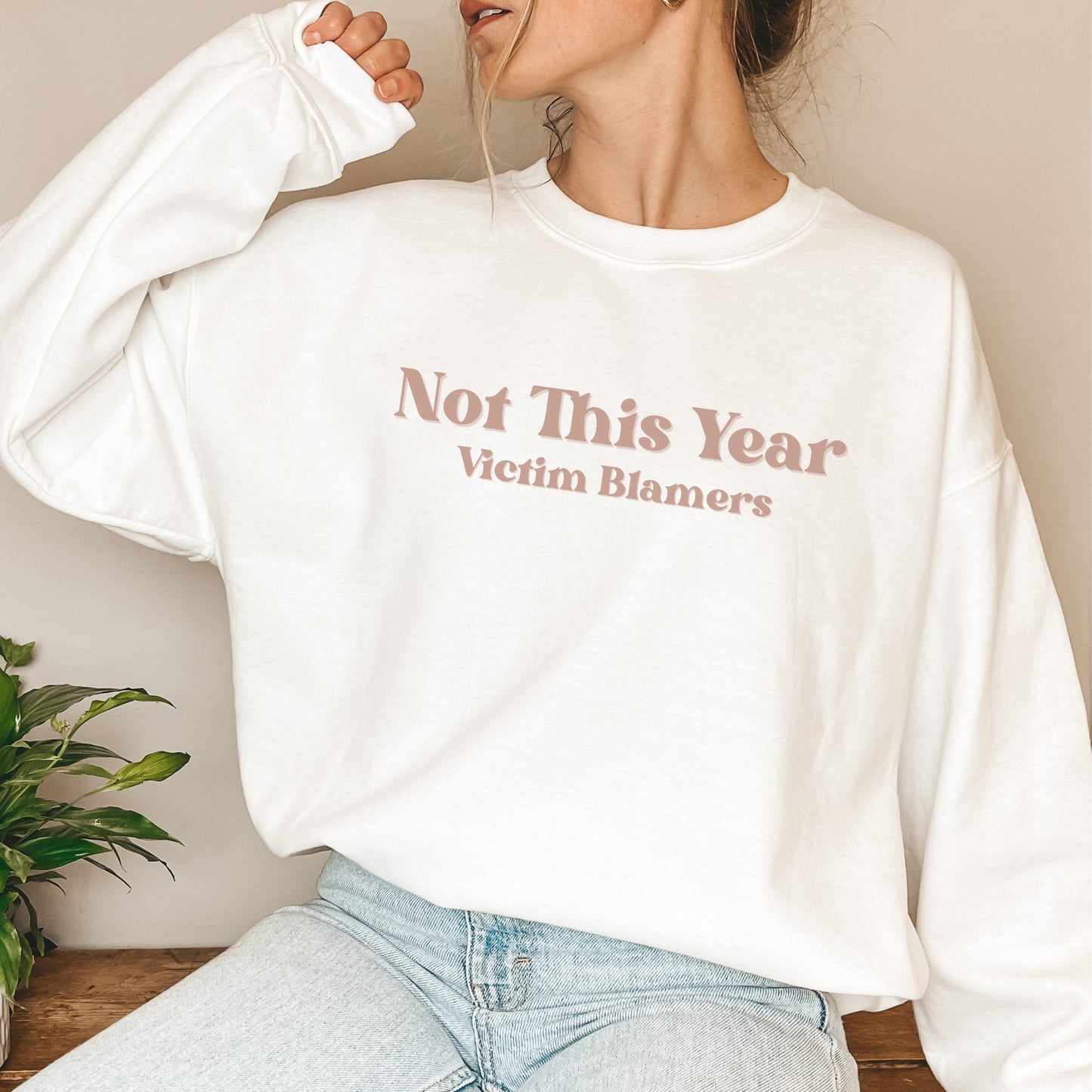 The front of the sweatshirt proudly displays the phrase "Not This Year Victim Blamers" in a bold and eye-catching font. This message serves as a reminder that we reject victim-blaming and support those who have faced injustice.