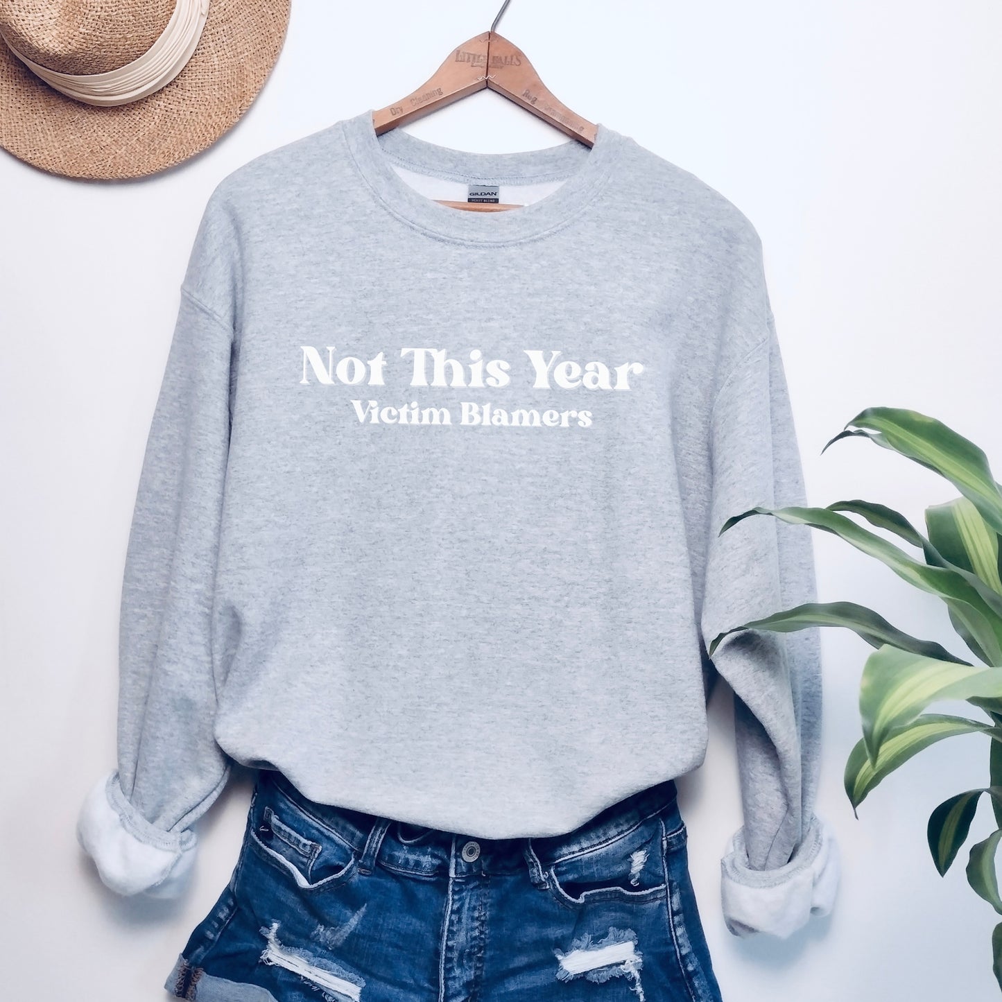 The front of the sweatshirt proudly displays the phrase "Not This Year Victim Blamers" in a bold and eye-catching font. This message serves as a reminder that we reject victim-blaming and support those who have faced injustice.
