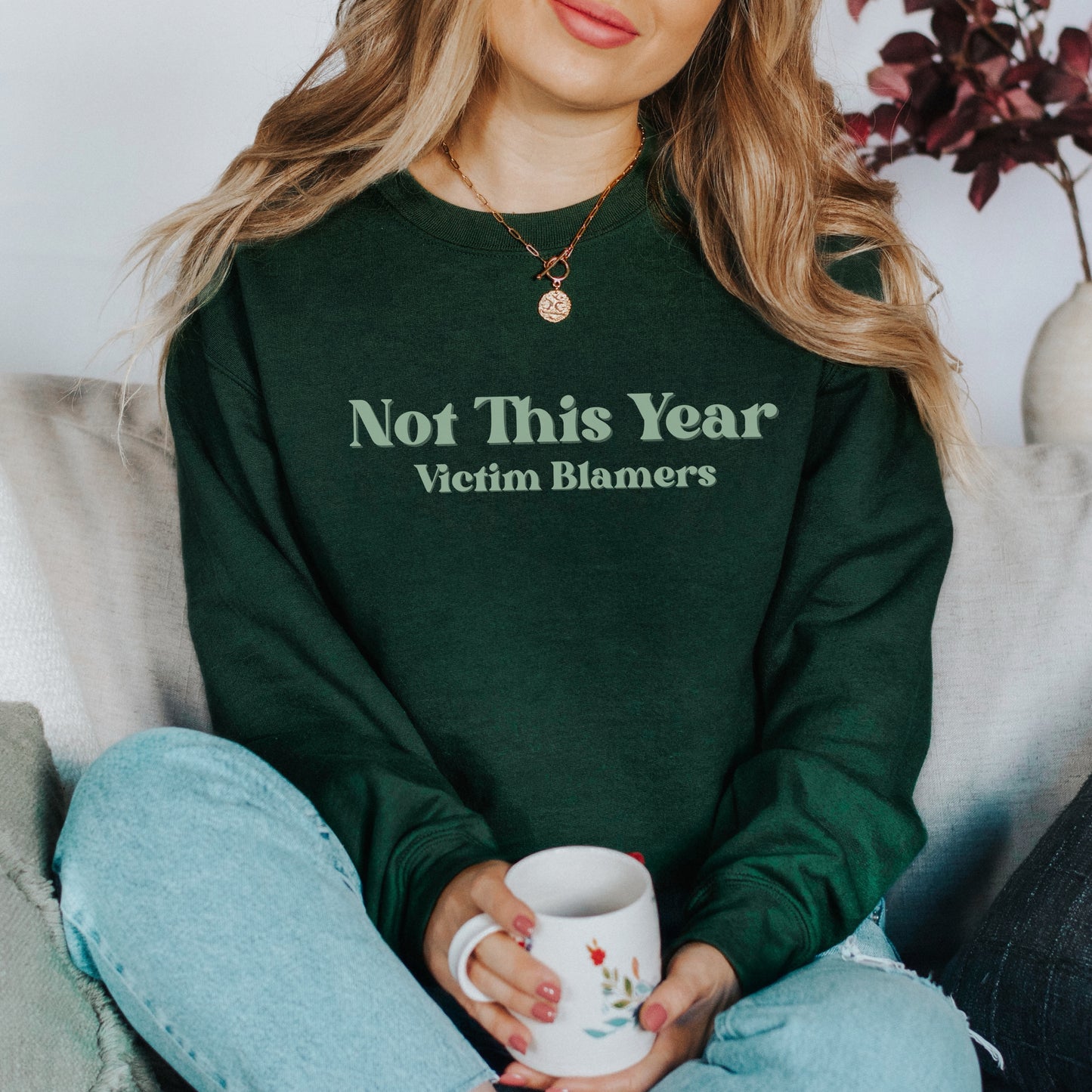 The front of the sweatshirt proudly displays the phrase "Not This Year Victim Blamers" in a bold and eye-catching font. This message serves as a reminder that we reject victim-blaming and support those who have faced injustice.