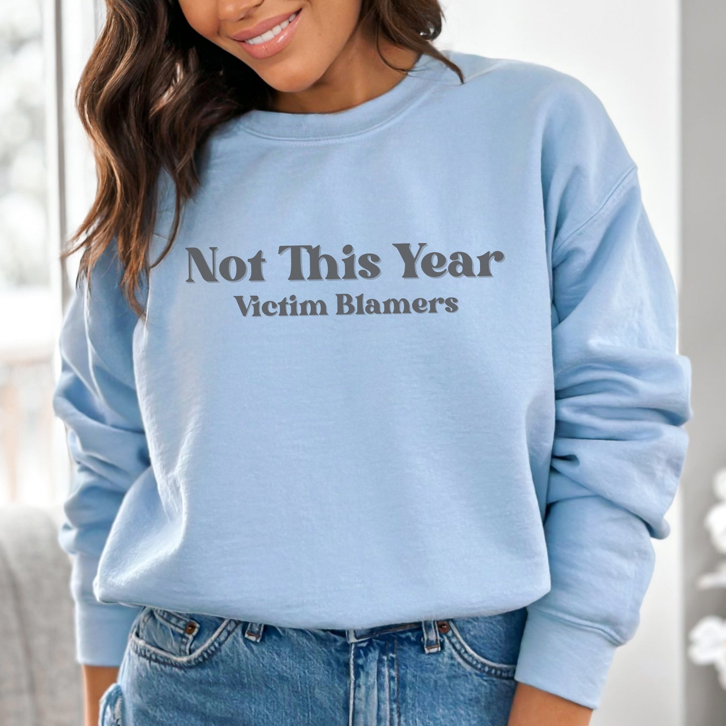 The front of the sweatshirt proudly displays the phrase "Not This Year Victim Blamers" in a bold and eye-catching font. This message serves as a reminder that we reject victim-blaming and support those who have faced injustice.