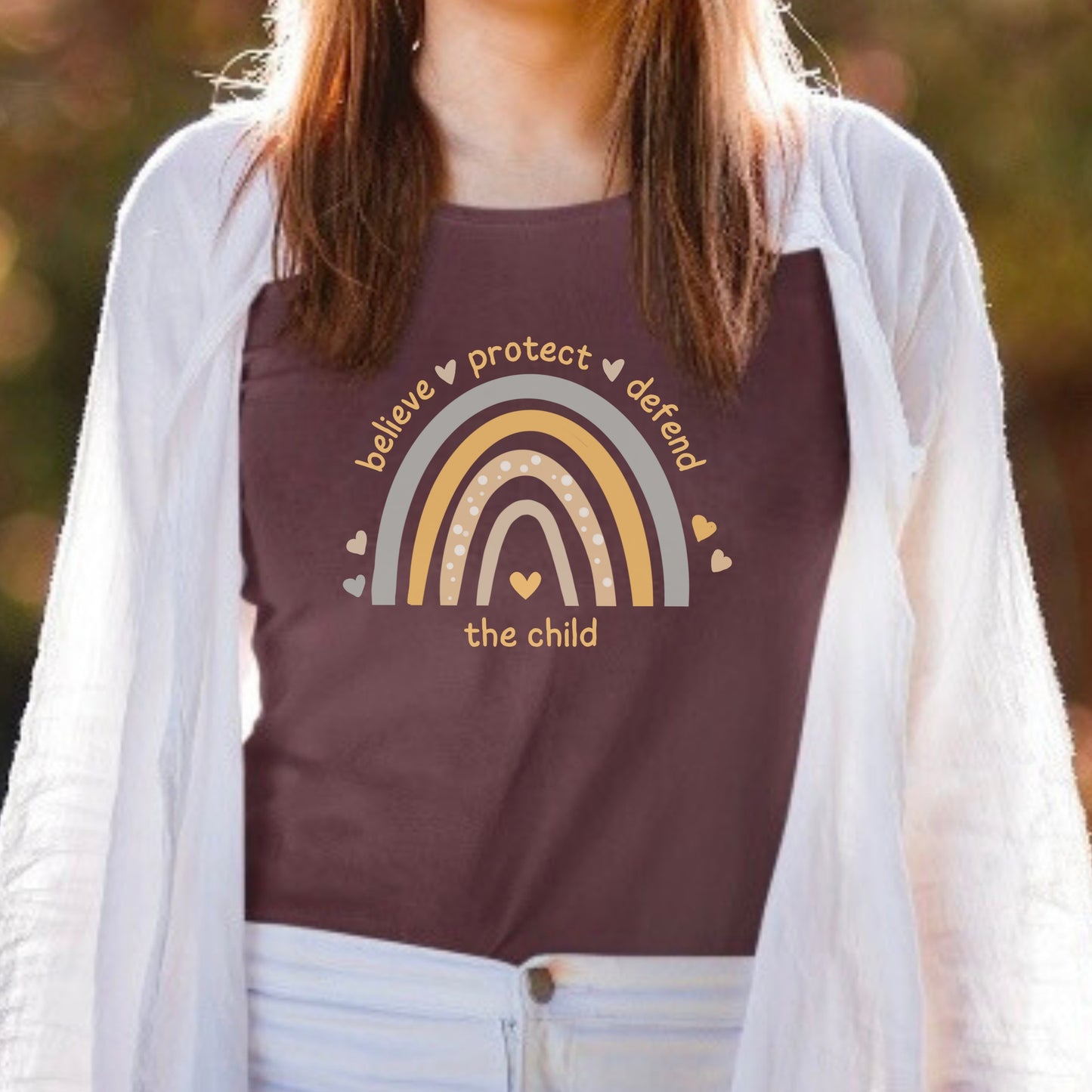 The front of the tee displays a boho rainbow with the phrase Believe Protect Defend The Child. A powerful message that underscores the importance of safeguarding children's rights and well being. Perfect for child advocates and Child Abuse Awareness and Prevention Month (CAAPM)