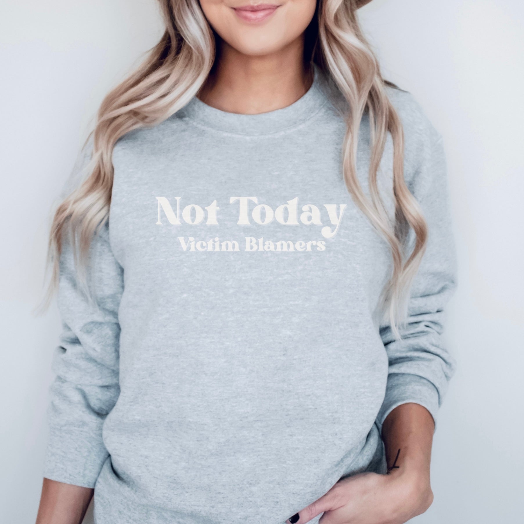 The front of the Sport Grey sweatshirt proudly displays the phrase "Not Today Victim Blamers" in a White bold and eye-catching font. This message serves as a reminder that we reject victim-blaming and support those who have faced injustice.