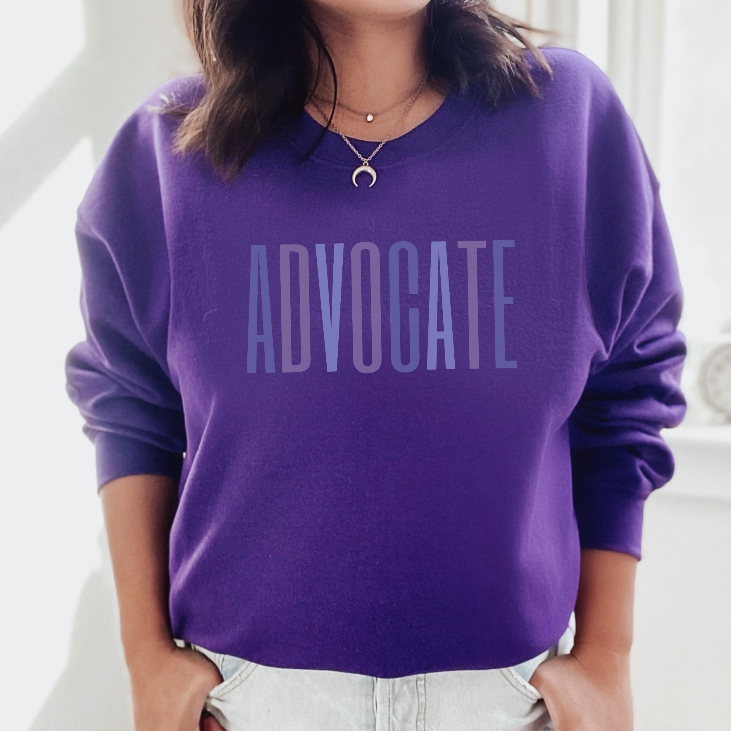 Purple crewneck sweatshirt with a powerful  "ADVOCATE" wordmark emblazoned across the chest in varying shades of purple, symbolizing the strength and unity of domestic violence advocates. The gradient effect from deep violet to lavender adds an eye-catching touch, making this sweater a visually compelling tribute to your commitment to ending domestic abuse.