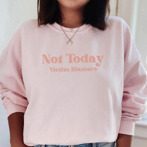 The front of the Light Pink sweatshirt proudly displays the phrase "Not Today Victim Blamers" in a melon color bold and eye-catching font. This message serves as a reminder that we reject victim-blaming and support those who have faced injustice.