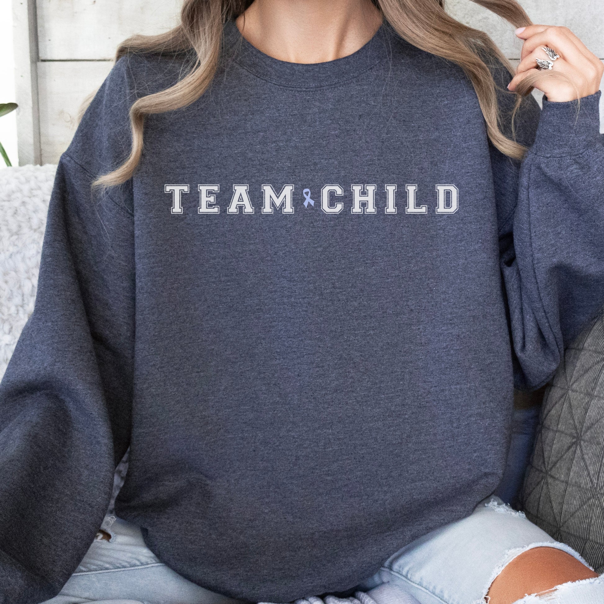 Our exclusive sweatshirt has ‘Team Child’ on the front in a bold font with the blue child abuse awareness ribbon between the words. This impactful phrase encapsulates the essence of your commitment to safeguarding children and promoting their well-being. Perfect for child advocates, champions of children’s mental health, and for Child Abuse Awareness and Prevention Month (CAPM)