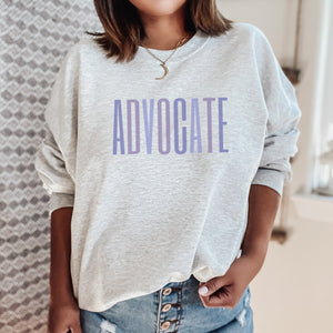 Ash crewneck sweatshirt with a powerful  "ADVOCATE" wordmark emblazoned across the chest in varying shades of purple, symbolizing the strength and unity of domestic violence advocates. The gradient effect from deep violet to lavender adds an eye-catching touch, making this sweater a visually compelling tribute to your commitment to ending domestic abuse.