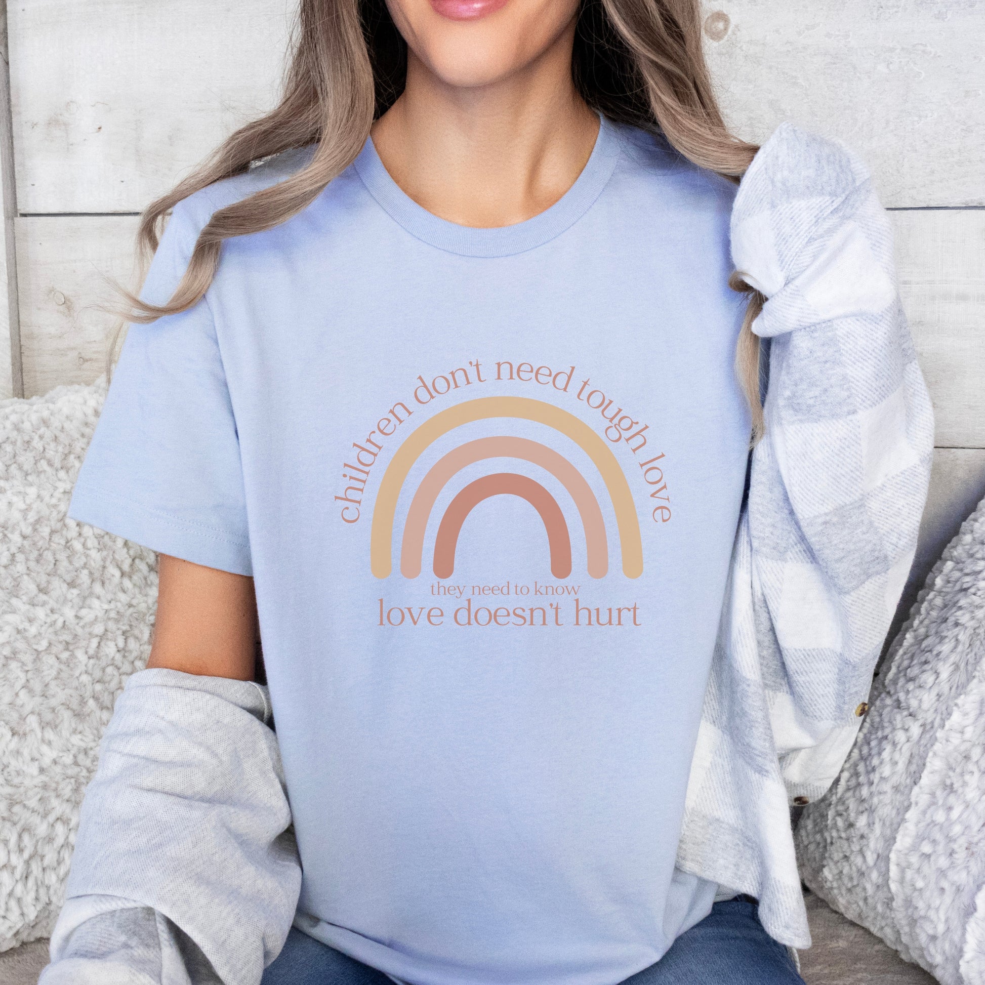 The front of the t-shirt has a beautiful boho rainbow that boldly declares, "Children don't need tough love, they need to know love doesn't hurt." It serves as a rallying cry for advocates, emphasizing the importance of fostering environments where love is synonymous with safety and support. Perfect for child advocates, family advocates, and Child Abuse Awareness and Prevention Month CAPM