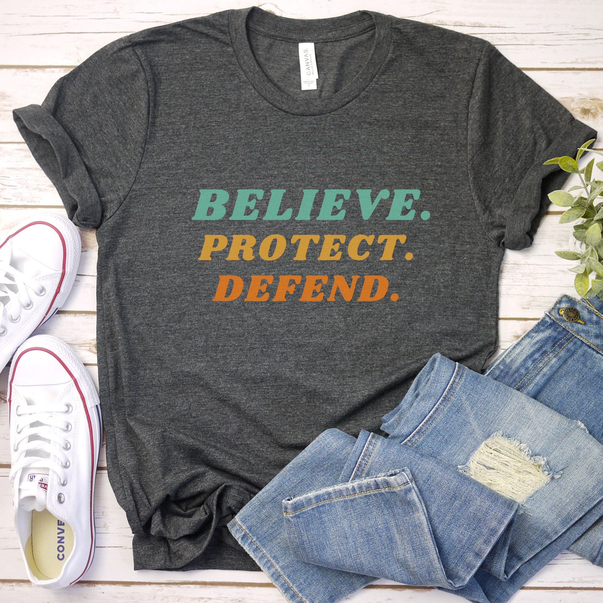 Dark Grey Heather Bella Canvas T-shirt with bold retro text in green, yellow, and orange that reads: Believe. Protect. Defend.