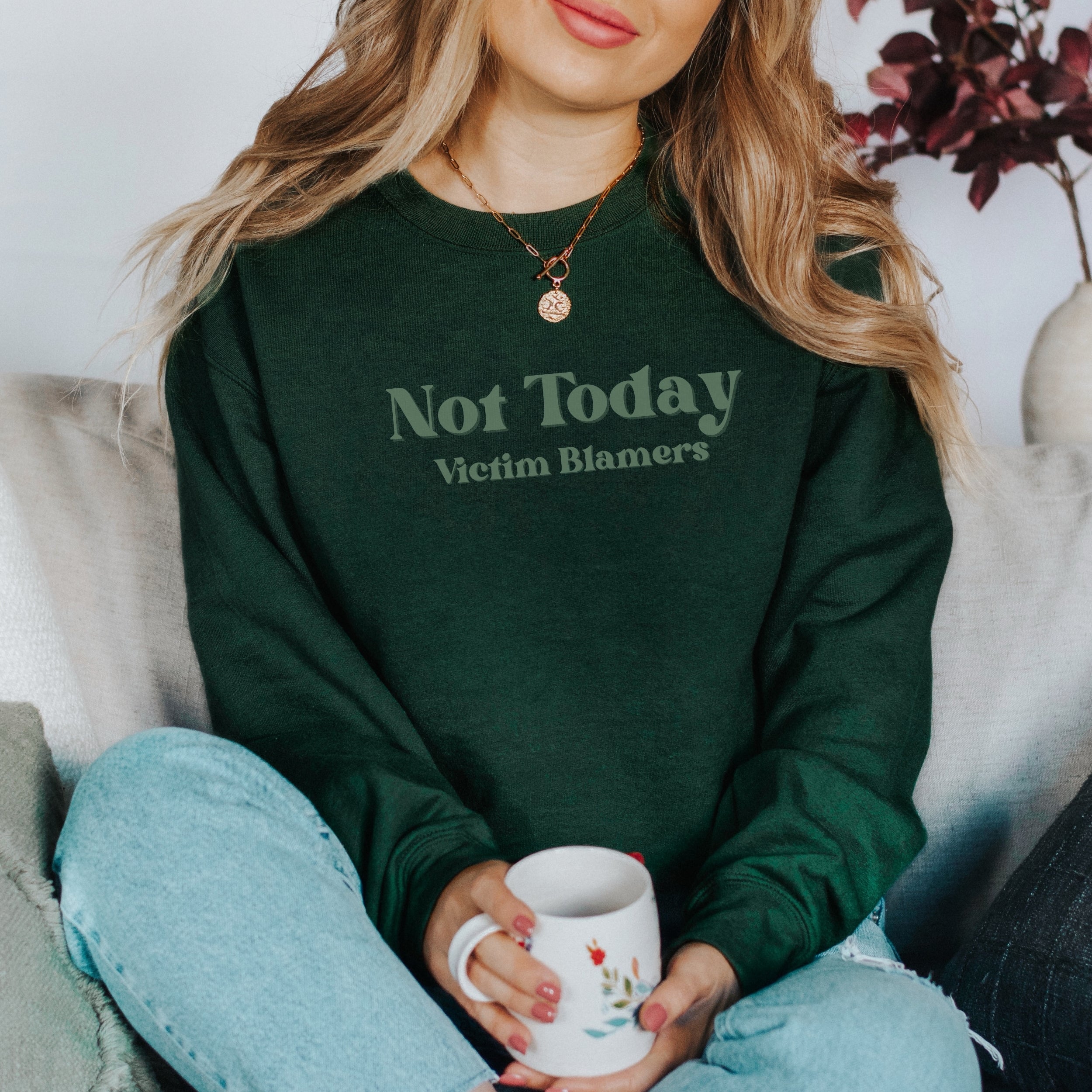 The front of the Forest Green sweatshirt proudly displays the phrase "Not Today Victim Blamers" in a Spruce colored bold and eye-catching font. This message serves as a reminder that we reject victim-blaming and support those who have faced injustice.