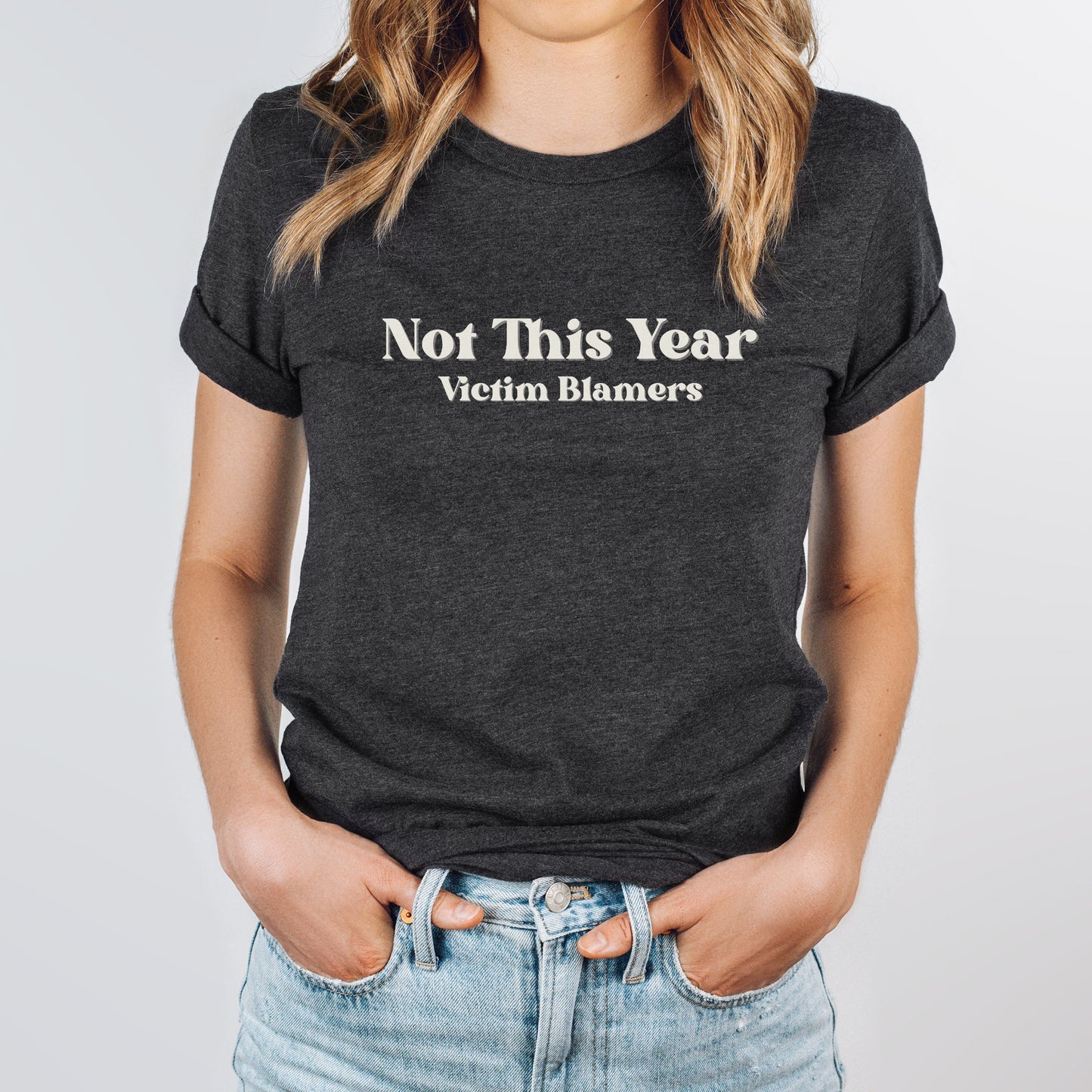 The front of the sweatshirt proudly displays the phrase "Not This Year Victim Blamers" in a bold and eye-catching font. This message serves as a reminder that we reject victim-blaming and support those who have faced injustice.