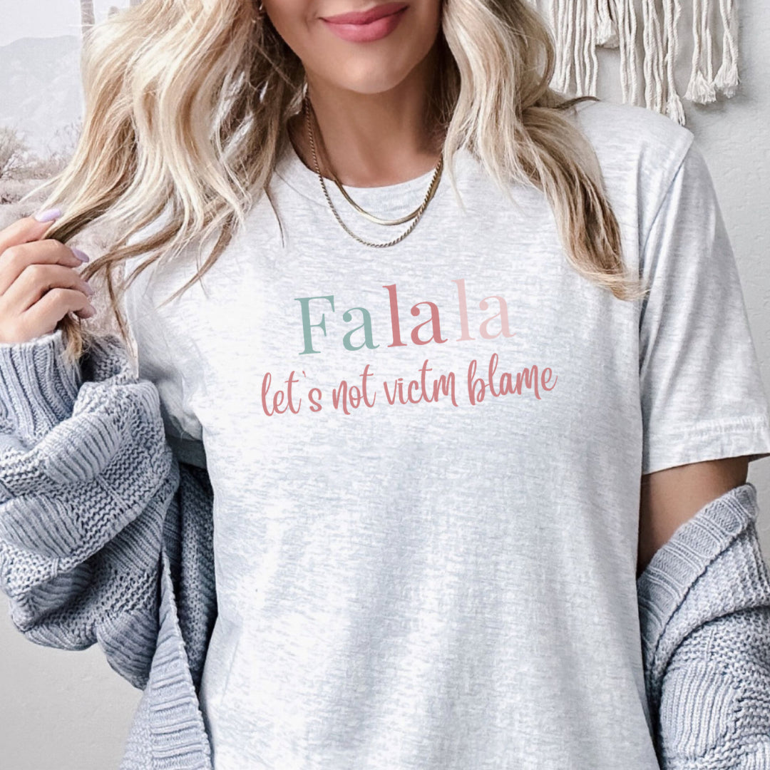 Empowerment-themed holiday T-shirt with festive trending colors design and the powerful statement 'Fa la la, Let's Not Victim Blame.' Ideal for advocates and survivors of abuse, this tee promotes empathy and awareness during the holiday season.
